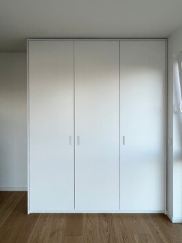 Kleiderschrank, weiß lackiert, mit rechteckigen Grifffräsungen.