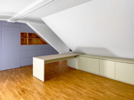 Schreibtisch und Schränke mit matter Oberfläche in grün und blau und Details aus Eiche unter einer Dachschräge.