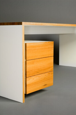 Schreibtisch, hell beschichtet, mit Kanten und Schubkastenblenden aus Massivholz.