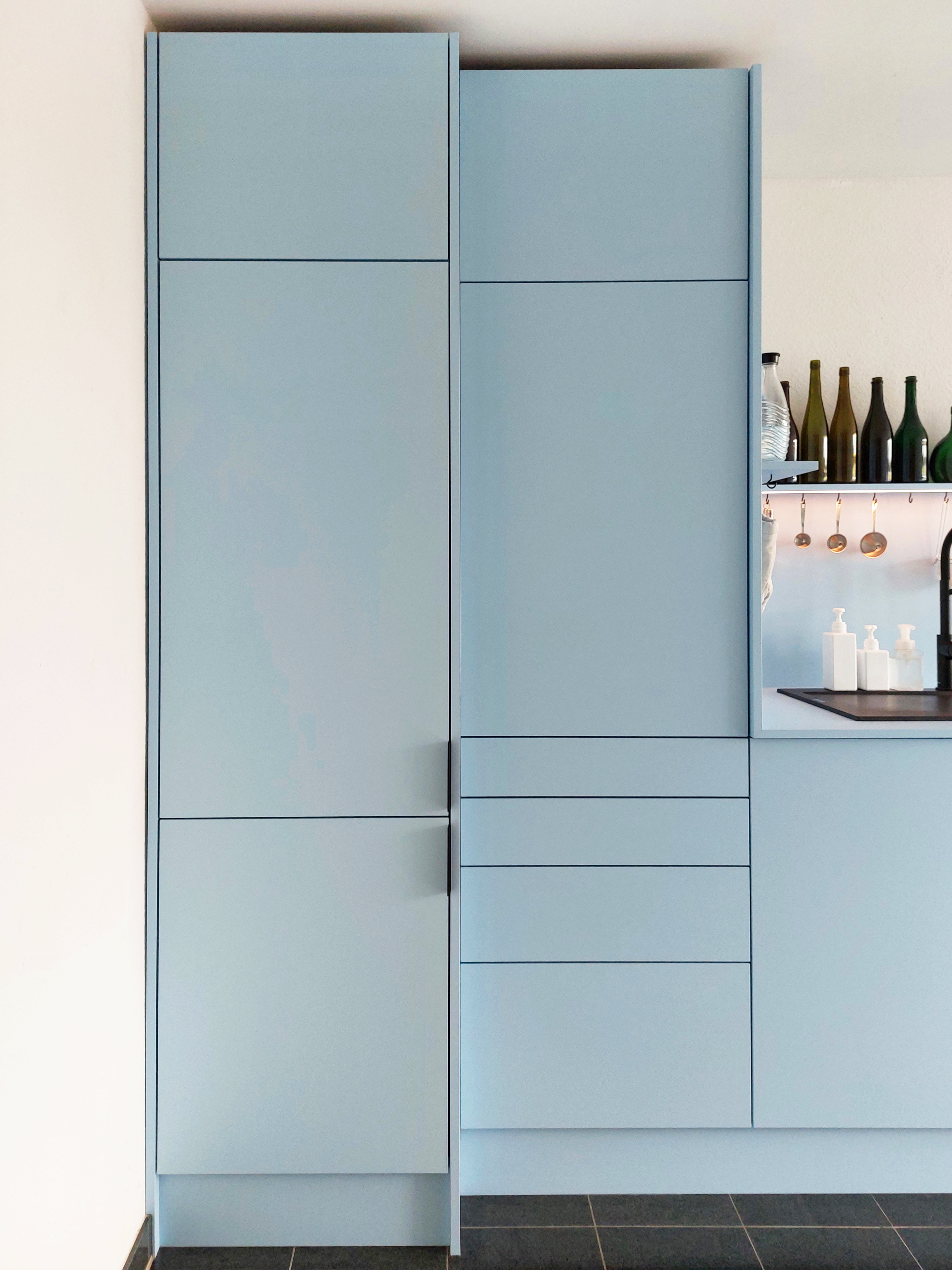 Küchenschrank in hellblau, matt, dezente schwarze Griffbleche. 