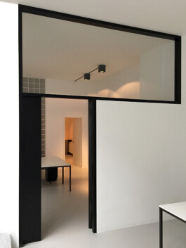 Weiße Trennwand zwischen Büroraumen mit schwarz gebeizter Tür und breites Oberlicht mit schwarzem Rahmen. Entwurf Rinnebach Architektur 