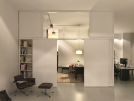 Büroraum aus weißen Elementen, teilweise mit Glas gefüllt, teilweise Schränke mit Schiebetüren. Entwurf Rinnebach Architektur 