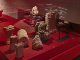 Roter Sockel mit Vitrine und antiken Fragmenten von Säulen und Statuen.
