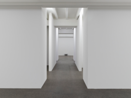 Installationsansicht in einen Gang aus weißen Wänden, von dem mehrere Räume abzweigen 
