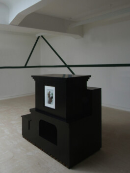 Schwarzes Objekt mit kleinem eingelassenen Bild in einem weißen Raum 