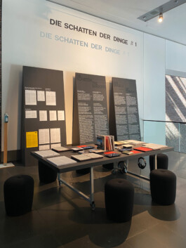 Dreieckige große Aufsteller mit Ausstellungstexten bedruckt, davor ein Tisch mit Literatur, alles aus schwarzem MDF 