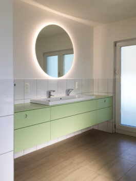 Pastellgrüner Waschtisch mit großem Waschbecken und rundem Spiegel. 