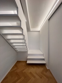 Weiße Treppe mit Podest, offener Setzstufe und geschlossener Brüstung. 