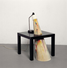 Lampe auf einem kleinen schwarzen Tisch. Der Lichtschein dargestellt durch einen schrägen bemalten Kegel, der durch die Tischplatte geht. 