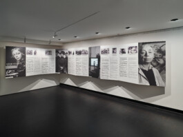 Großes Leporello (aufgefaltetes Papierband) entlang der Wand eines Ausstellungsraumes, dass mit schwarz-weiß Fotografien und Daten aus dem Leben von Käthe Kollwitz zeigt.