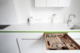 Weiße Küche mit grünem Griffdetail, Arbeitsplatte aus Corian und Schubkästen aus Massivholz. 