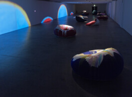 Dunkler Raum mit bunten Projektionen auf den Wänden und runden bunten Objekten auf dem Boden 