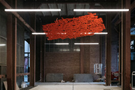 Rote Skulptur, die unter der Decke einer Industriehalle hängt. Die Skulptur ist ein flächiges Netz verzweigter Linien, dass aus der Kartierung ehemaliger Stollensysteme unter dem Ruhrgebiet abgeleitet ist.