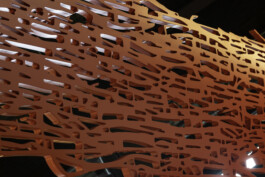 Detailansicht einer roten Skulptur. Die Skulptur ist ein flächiges Netz verzweigter Linien, dass aus der Kartierung ehemaliger Stollensysteme unter dem Ruhrgebiet abgeleitet ist. Licht scheint durch die Zwischenräume und wird von der Oberfläche matt reflektiert.