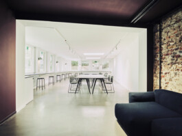 Blick in hellen langen Raum mit hellgrauen Tischplatten und schwarzen Tischgestellen.