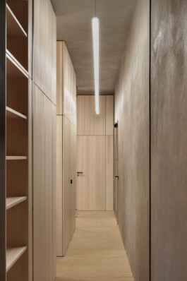 Schmaler, hoher Flur mit Lehmputz und raumhohen Einbauten aus Dreischichtplatte und schmaler Röhren-Leuchte. 
