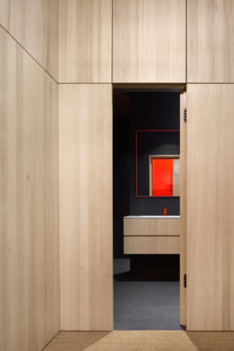 Blick in dunkles Badezimmer mit Waschtisch aus Weißtanne, freistehender Badewanne und Akzenten in orange. 