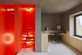 Leuchtend orangenes offenes Treppenhaus mit Ringleuchte und einem Raum mit Schreibtisch und Lehmputz. 