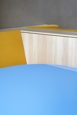 Detailaufnahme von den Materialien: Lehmputz, grobgewebter gelber Stoff, Weißtanne und Hochglanzlack in hellblau. 