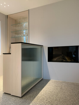 Theke aus zwei ineinander gestellten Weißtanne-Korpen mit einer Front aus einem spiegelnden Strukturglas, dessen Kanten über ein LED Band beleuchtet werden können. Die Arbeitsflächen aus schwarzer Steinplatte.